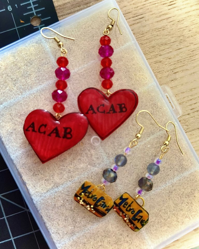  two pair of earrings, one w. beads and red "ACAB" heart charms and one w. mini metrocard charms