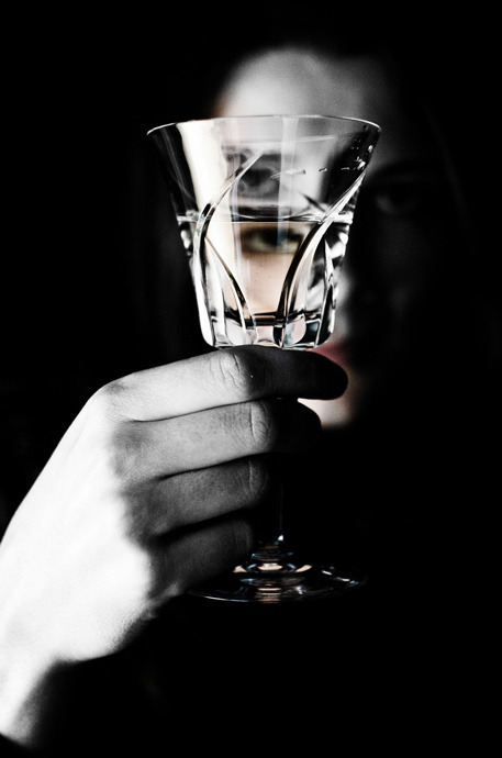 Hand holding a crystal wine glass with a silhouette of a woman in the dark background.