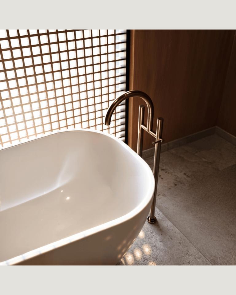 Minimalist white freestanding bathtub, bronze floor-mounted faucet.