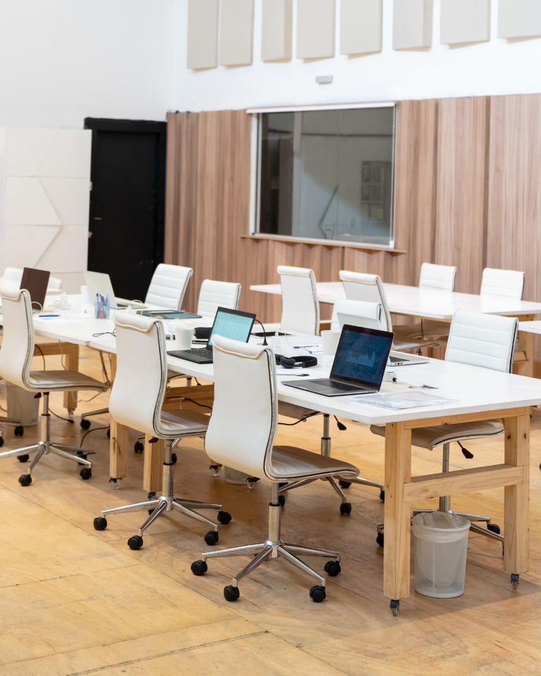 Modern shared office space with white ergonomic chairs, wooden desks, and laptops for co-working.