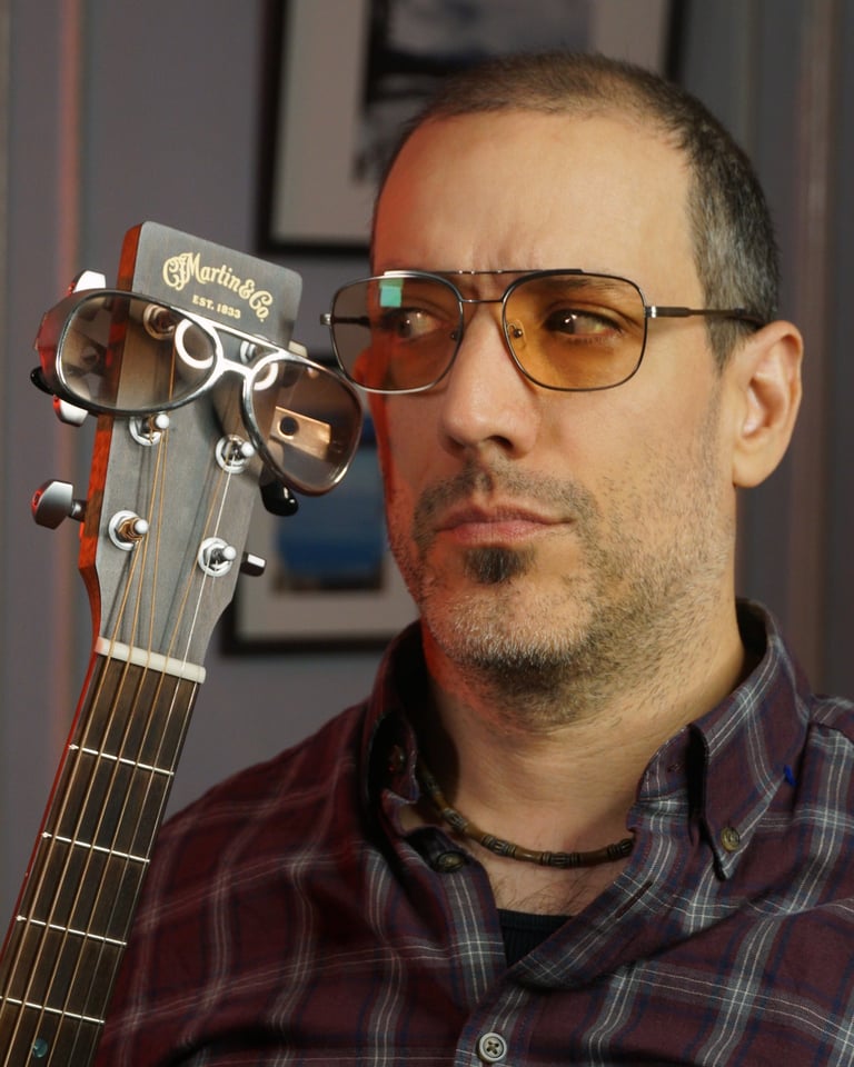 Closeup of Rob wearing aviator tinted glasses, looking at the headstock of his guitar, also sporting