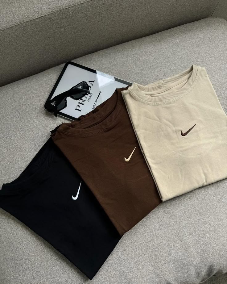 Tres sudaderas Nike de cuello redondo dobladas en colores neutros.