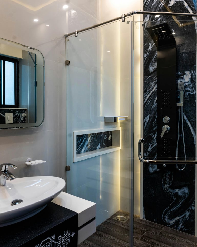 Baño reformado en Valencia con detalles en mármol negro, ducha de cristal y diseño elegante.