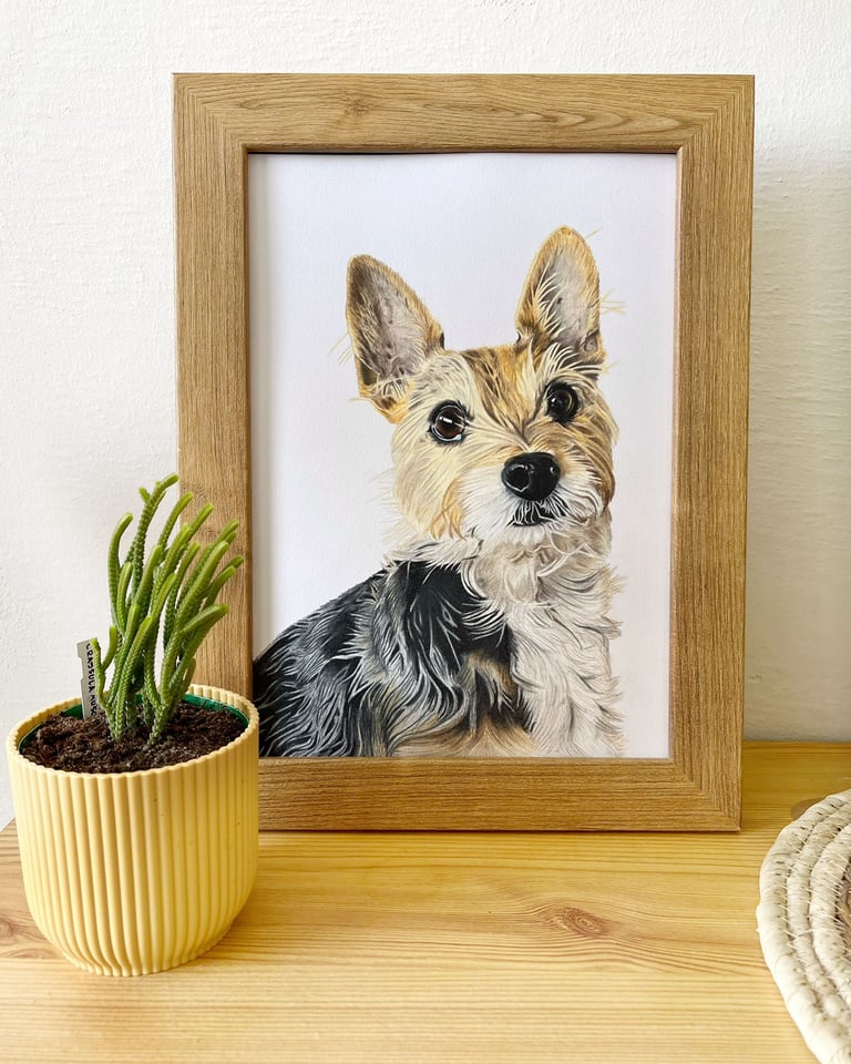 Custom framed terrier pet portrait painting on a wooden shelf next to a small potted cactus.