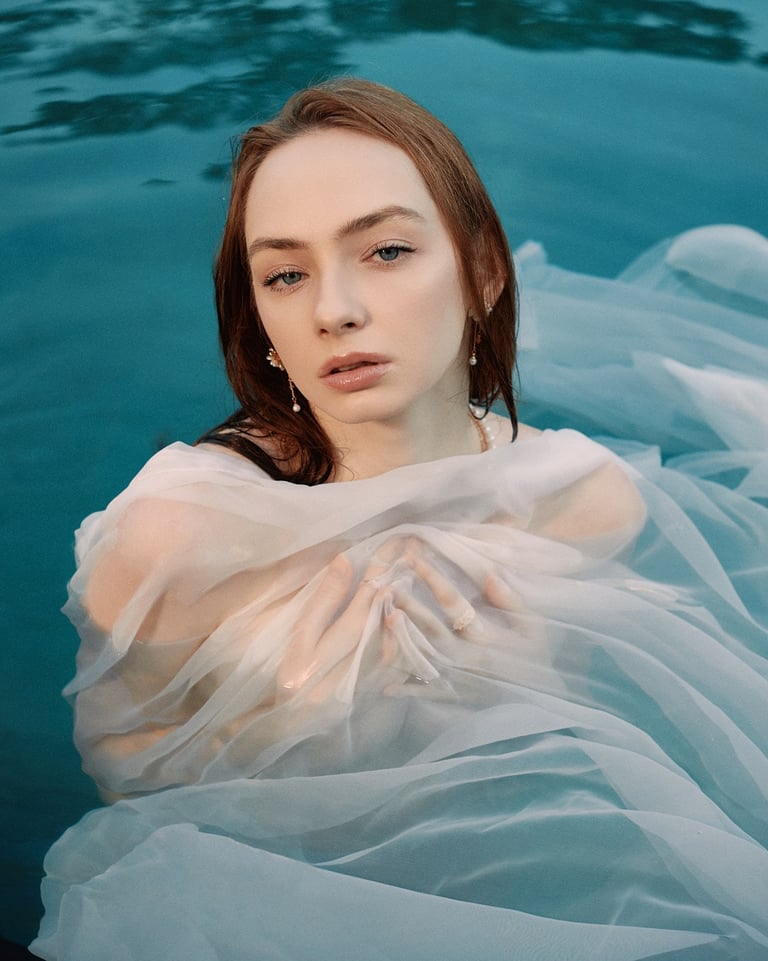 Portrait of Angelika partially submerged in water, wrapped in sheer fabric and lit by natural light.