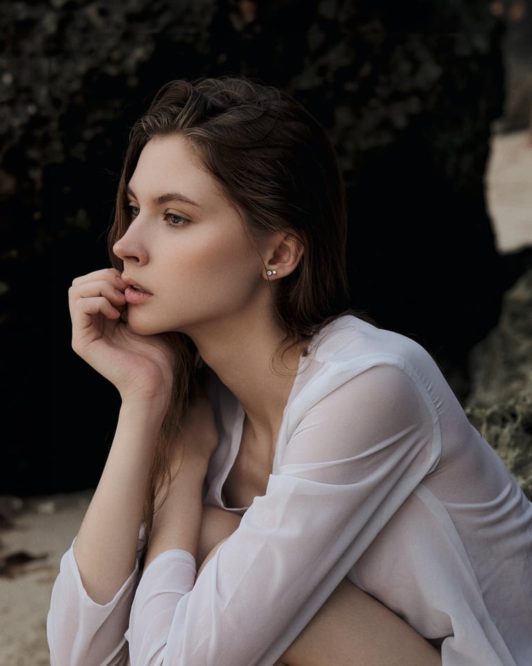 Side-profile portrait of Arisha seated outdoors, resting her face on her hand in soft natural light.