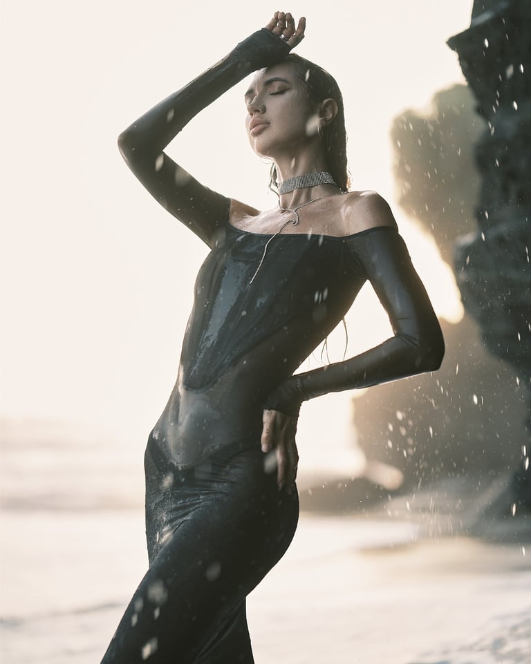 Portrait of Elena standing near the shoreline, photographed under rain and appearing wet in natural light.
