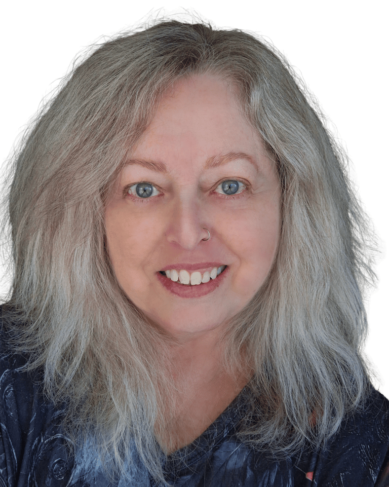 A middle aged woman with green eyes and blonde hair and wearing a grey patterned top