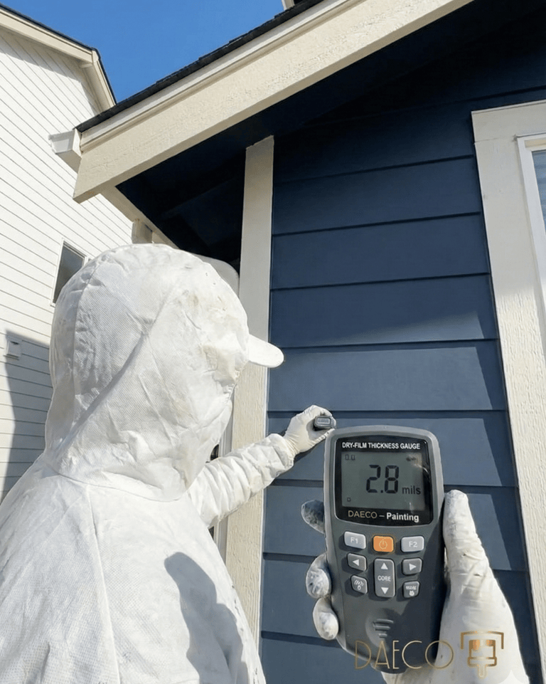 a person in a white painter suit measuring paint thickness - daeco paintng