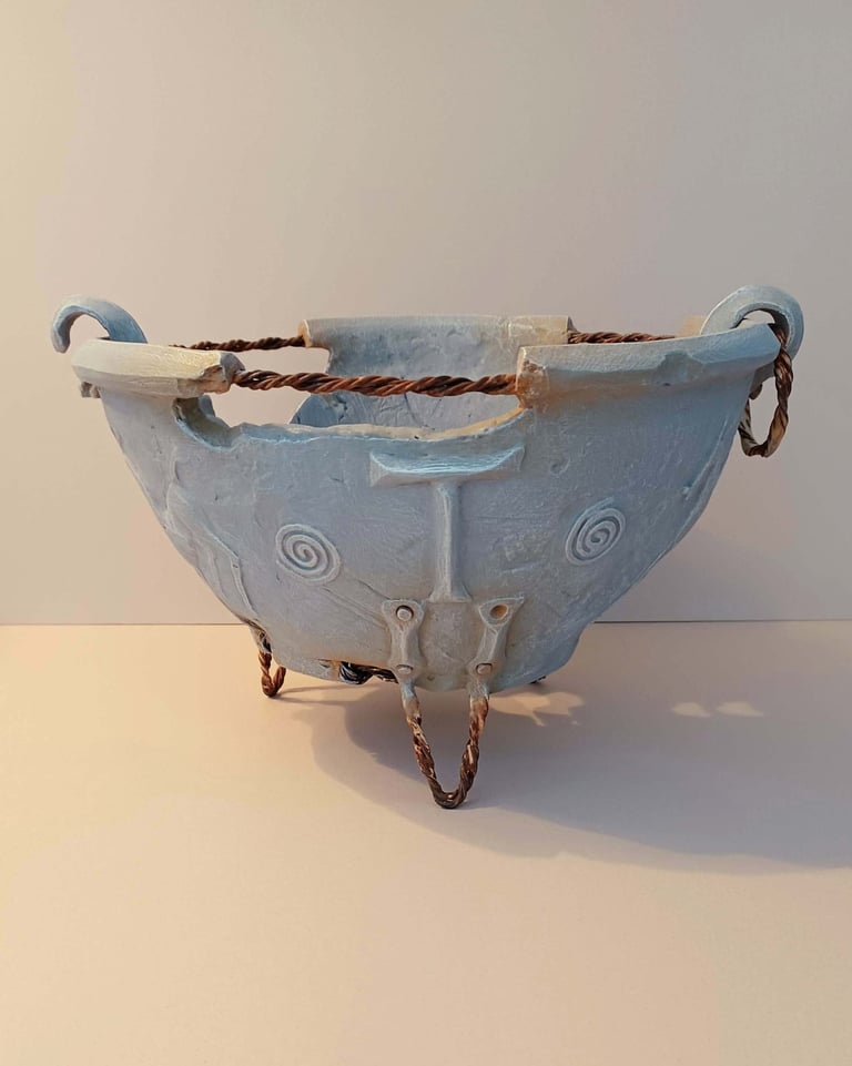 A fragmented, round bowl-like sculpture adorned with symbols and letters, finished in blue-grey hues