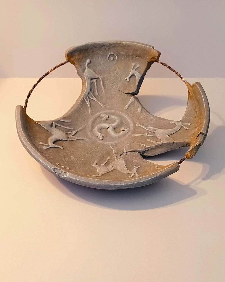 A fragmented bowl-like sculpture with embossed horse figures and symbols in rust/brown hues