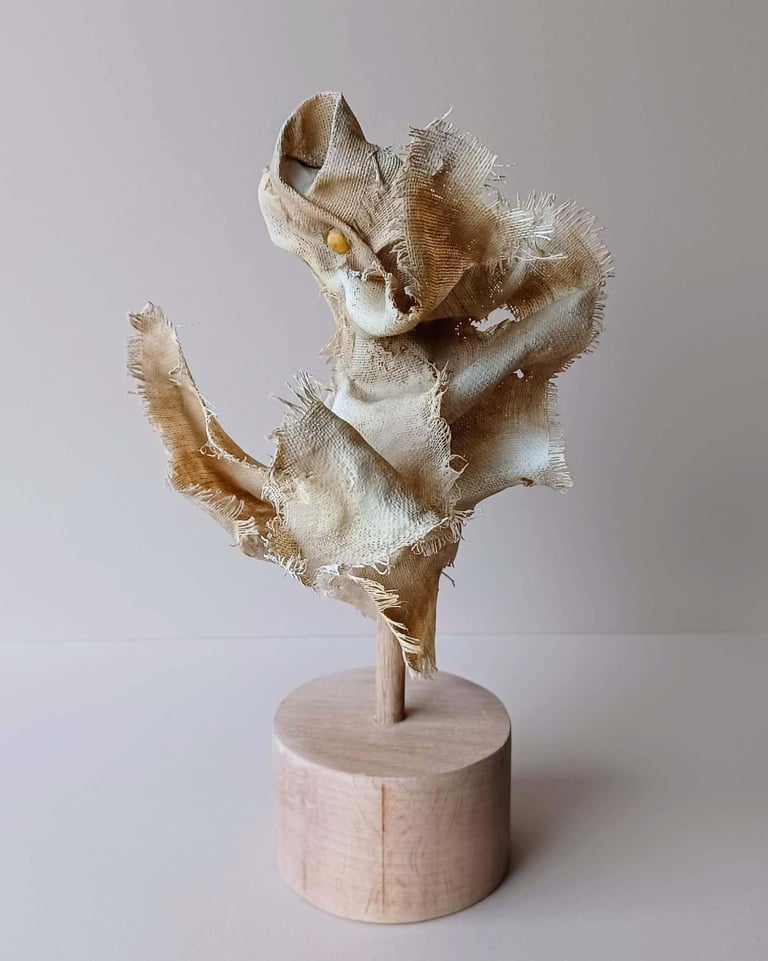 Rear view, showing a clay and canvas sculpture of a female torso, with windswept, ragged clothes.