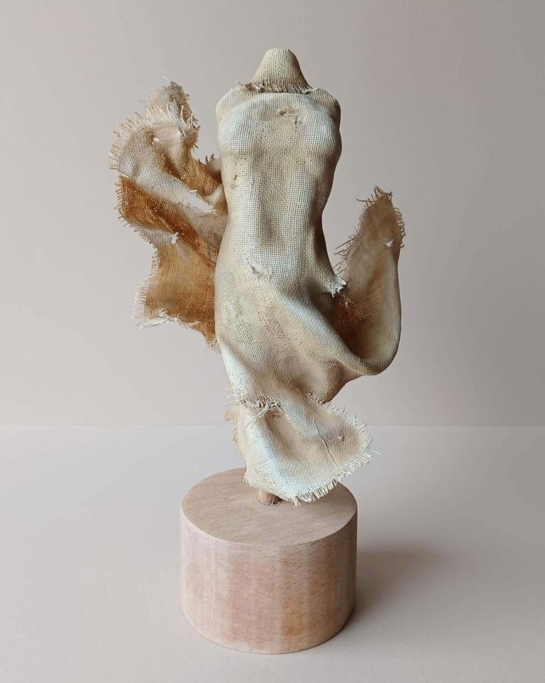 Clay and canvas sculpture of a female torso, wearing windswept, ragged clothes.