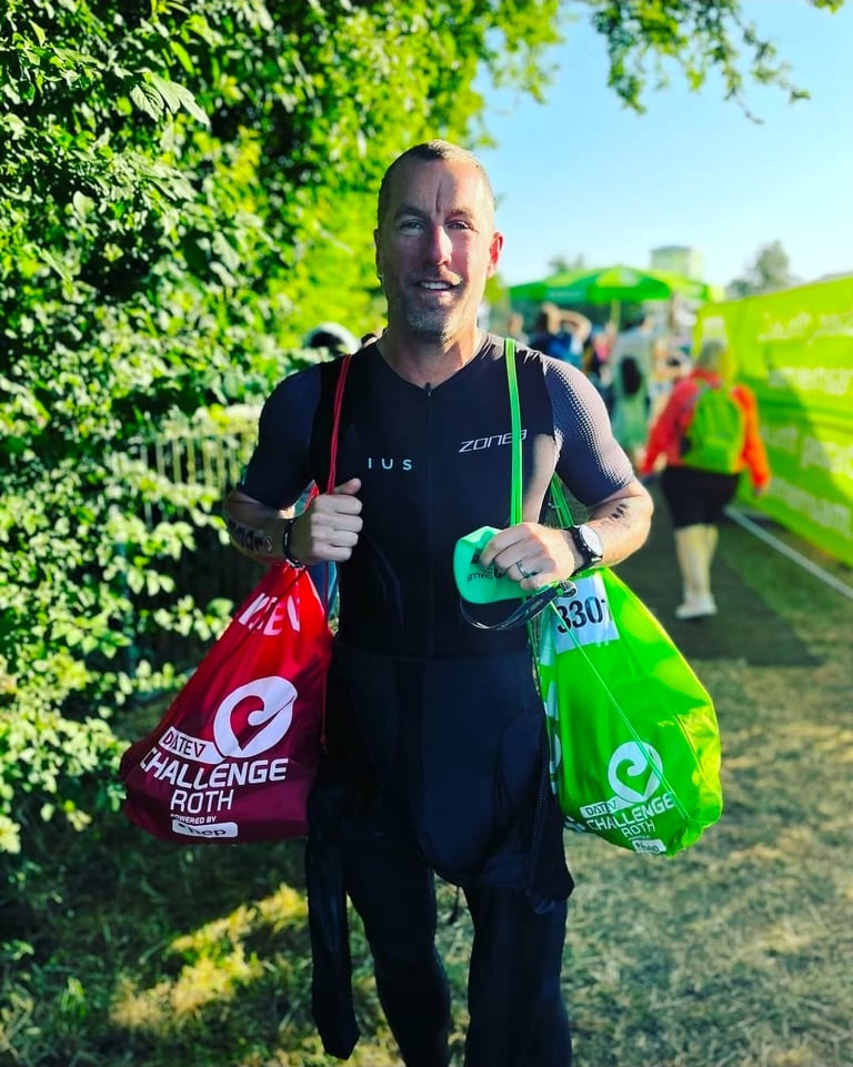 A male triathlete carrying red and green transition bags at the DATEV Challenge Roth triathlon event.