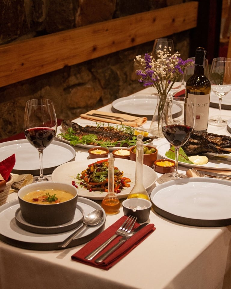 Gourmet dinner table with red wine, grilled fish, appetizers, and soup at a rustic restaurant.