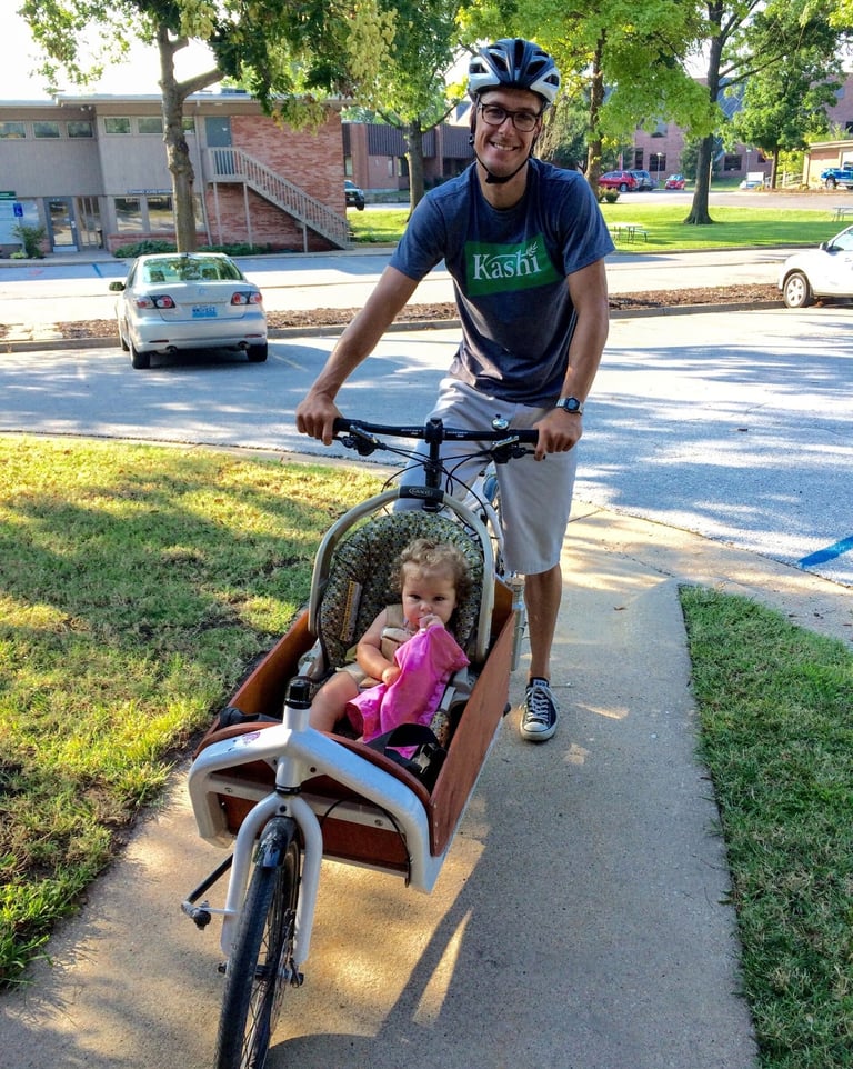 Man stopped posing on his bike, with a small carrier in the front holding a baby