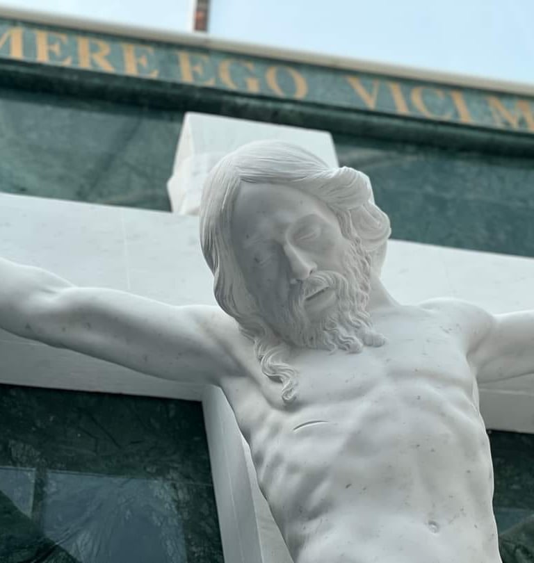 White marble Jesus Christ crucifixion statue on a cemetery headstone with Latin inscription.