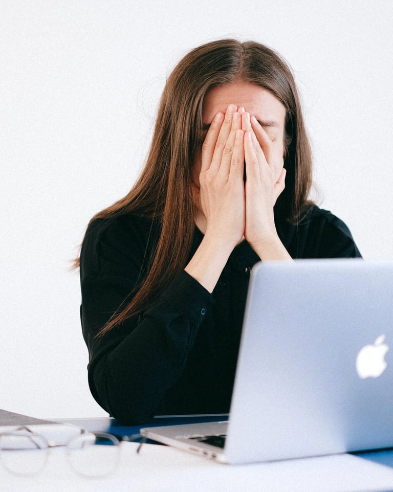 Une femme assise à son bureau se cache le visage avec ses mains devant son ordinateur
