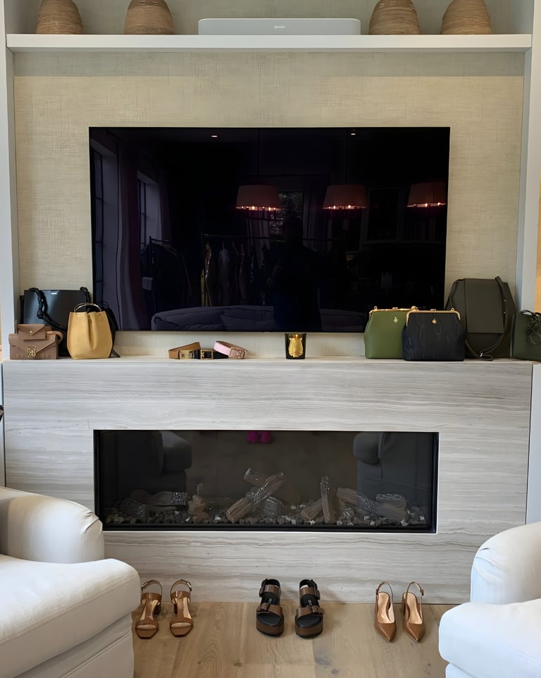 A refined display of luxury handbags and shoes by London stylist arranged along a fireplace ledge.