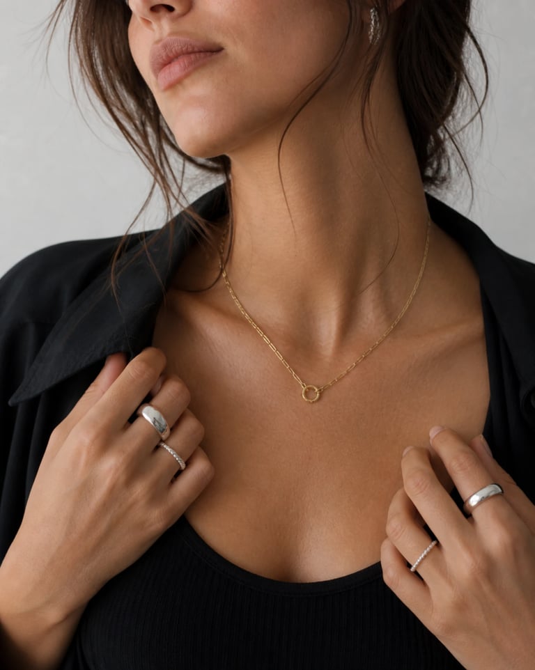 A woman wearing a delicate gold paperclip chain necklace with silver rings and a black blouse.