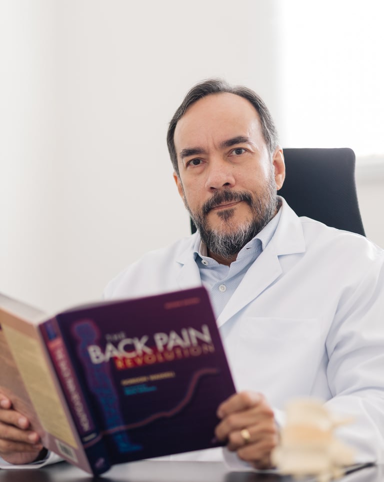 Neurocirurgião Dr. Carlos Moreira especialista em coluna lendo livro sobre dor em consultório.