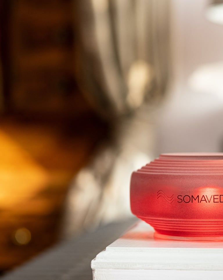 A glowing red Somavedic EMF mitigation device on a white nightstand in a cozy bedroom.
