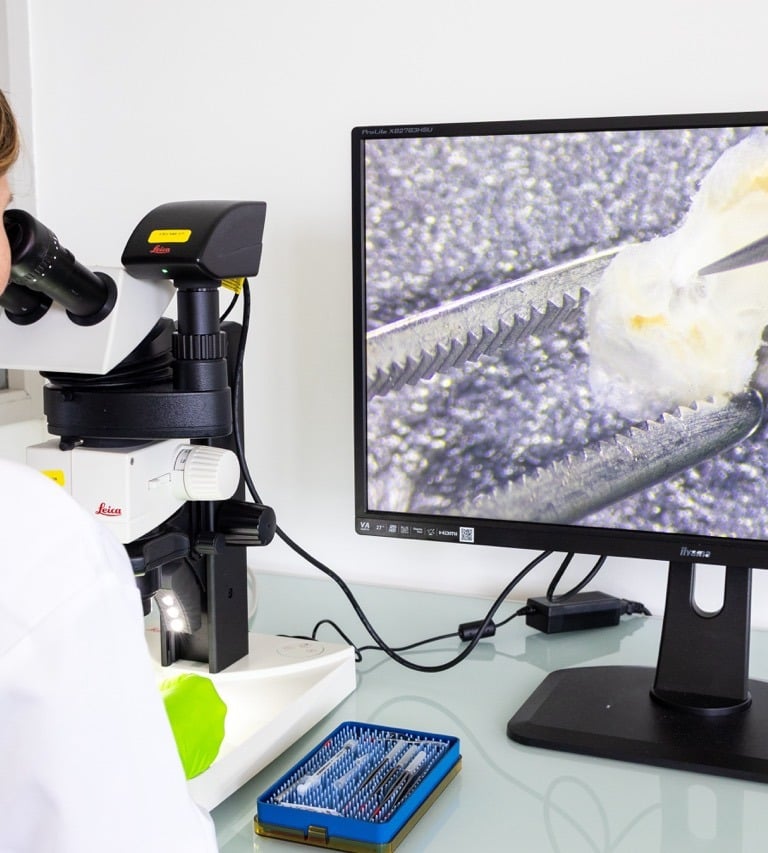 A scientist uses a Leica digital microscope to examine a sample displayed on a large computer monitor.