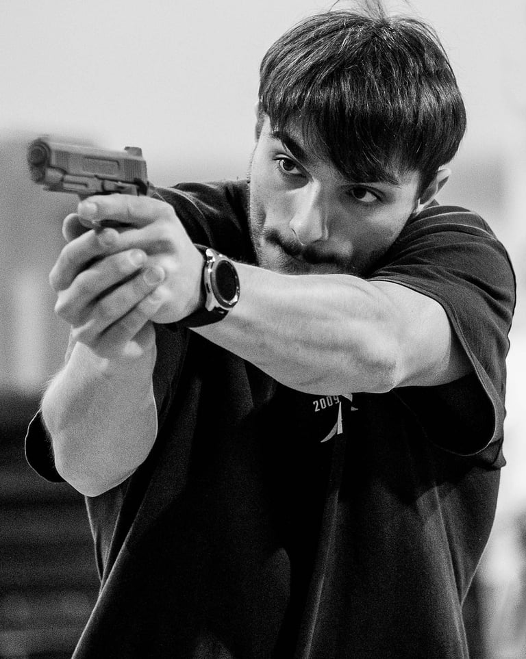 Stuntman with arms outstretched looking down the barrel of a pistol towards the left of the image 