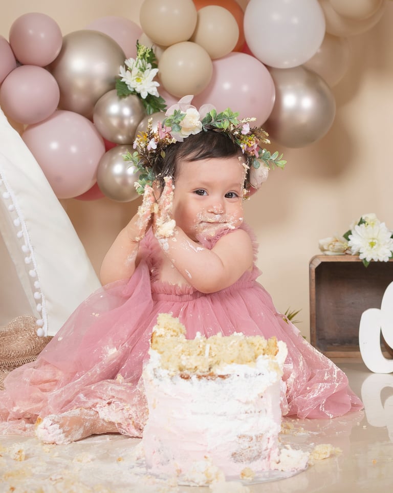 a baby girl in a pink dress and a cake
