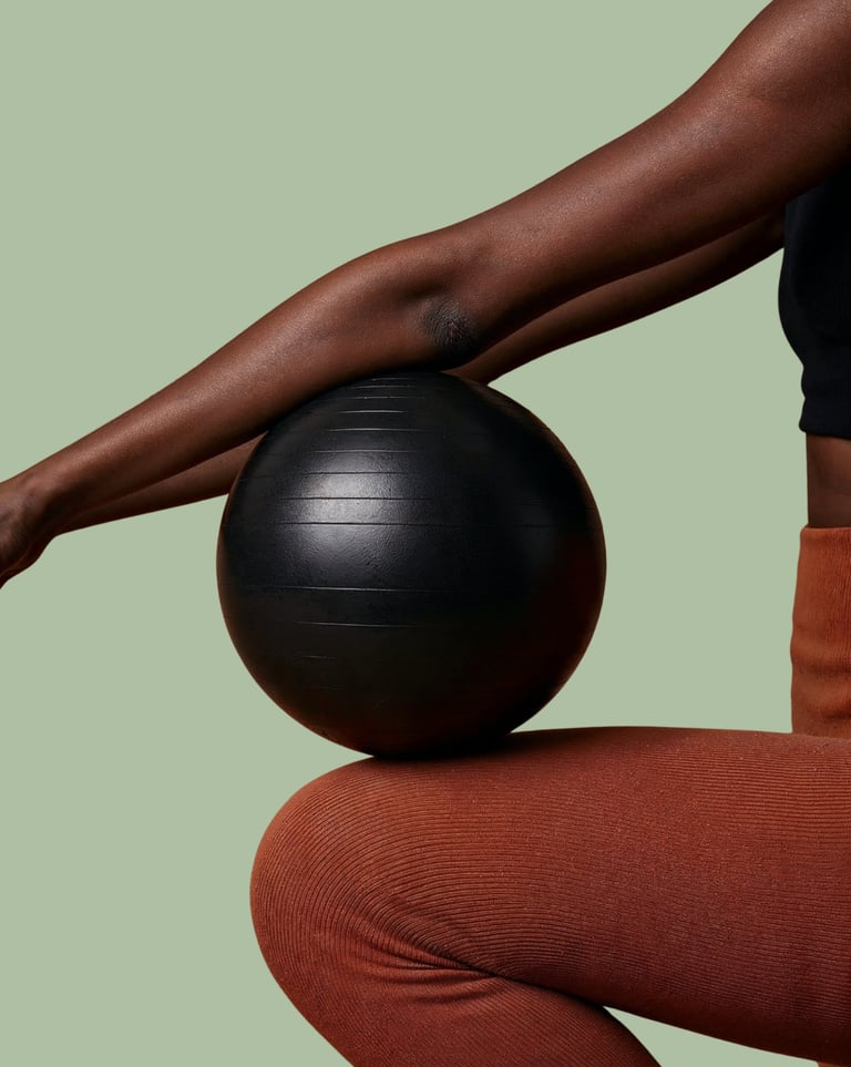Dark brow arms balance a black weighted medicine ball on their knee for core and stability training.
