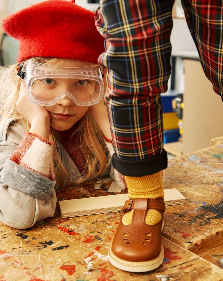 A young girl with a red beret and lab goggles, and a child on a table wearing Young Soles shoes