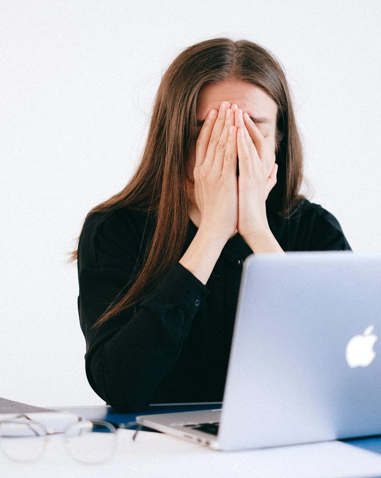 Une femme assise à son bureau se cache le visage avec ses mains devant son ordinateur