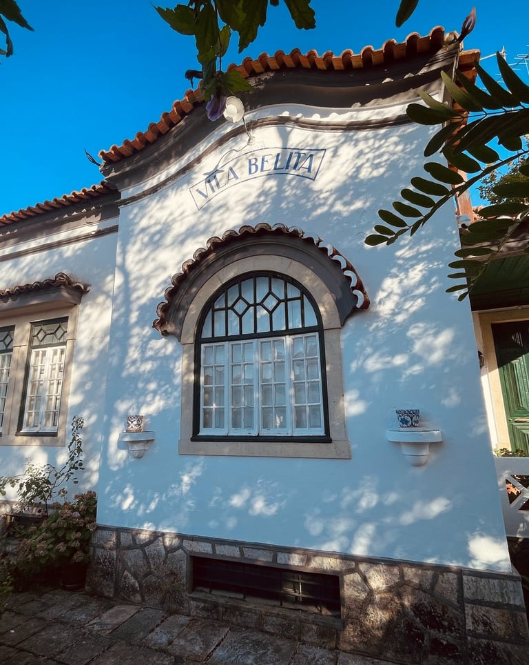 Traditional white Portuguese villa with arched windows, red tile roof, and green door in sunlight.