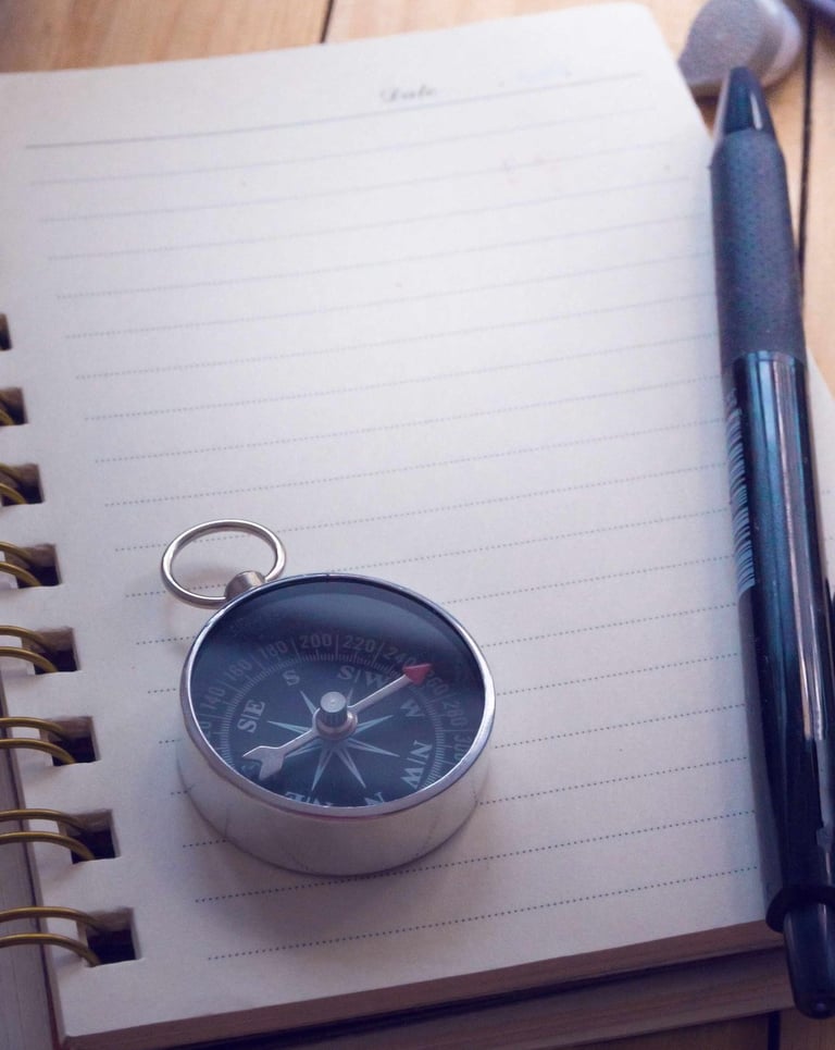 A compass on top of a notebook, with a pen and camera on the side