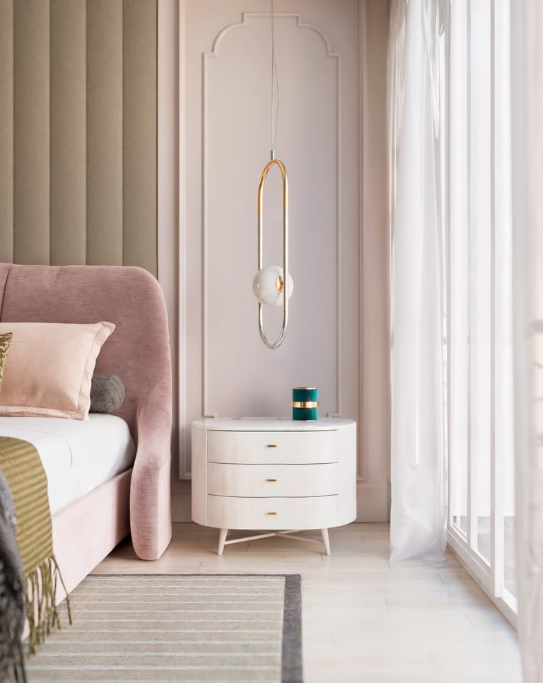 Modern pink velvet bed next to a white three-drawer nightstand and elegant gold pendant lighting.