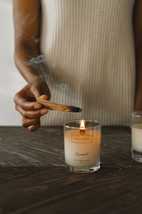brown skin woman lighting palo santo stick in a candle
