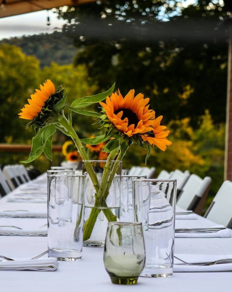 Elegant outdoor dining table set with white linens and sunflower centerpieces for a wedding reception.