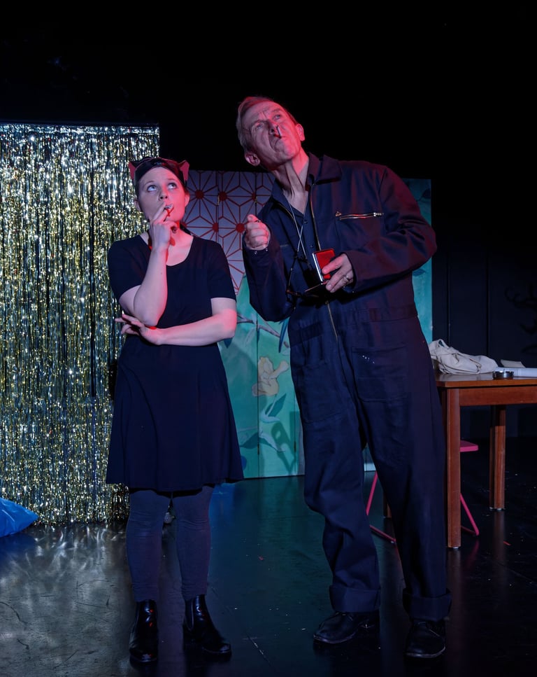 Zwei Schauspieler:innen rauchen vor einem glitzernden Vorhang.