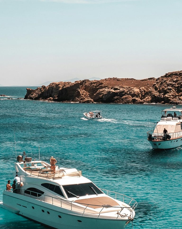 Boats floating on clear blue sea near rocky coast.