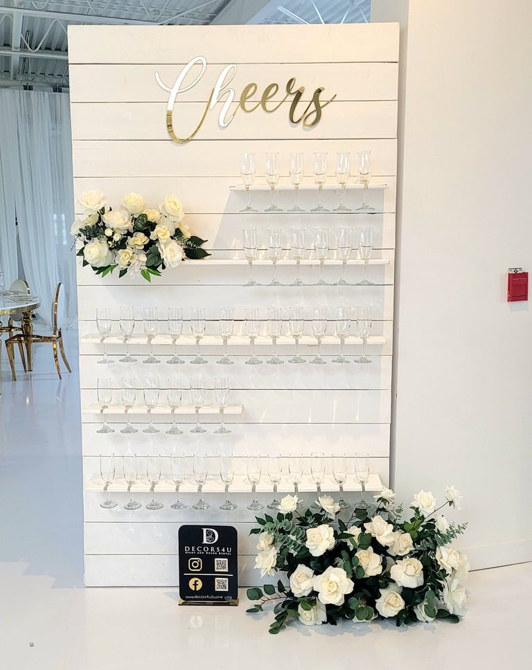 White champagne with white roses and greenery flowers and a sign that says cheers