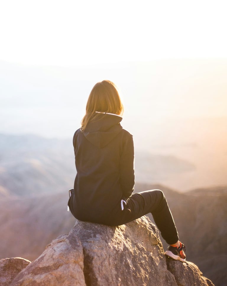 Solo traveler seated on a mountaintop, gazing at a serene sunset view.