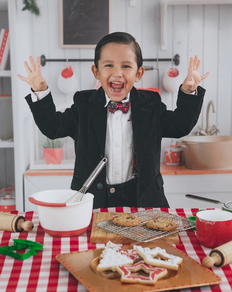 un niño con smoking sonriendo a la cámara frente a galletas navideñas