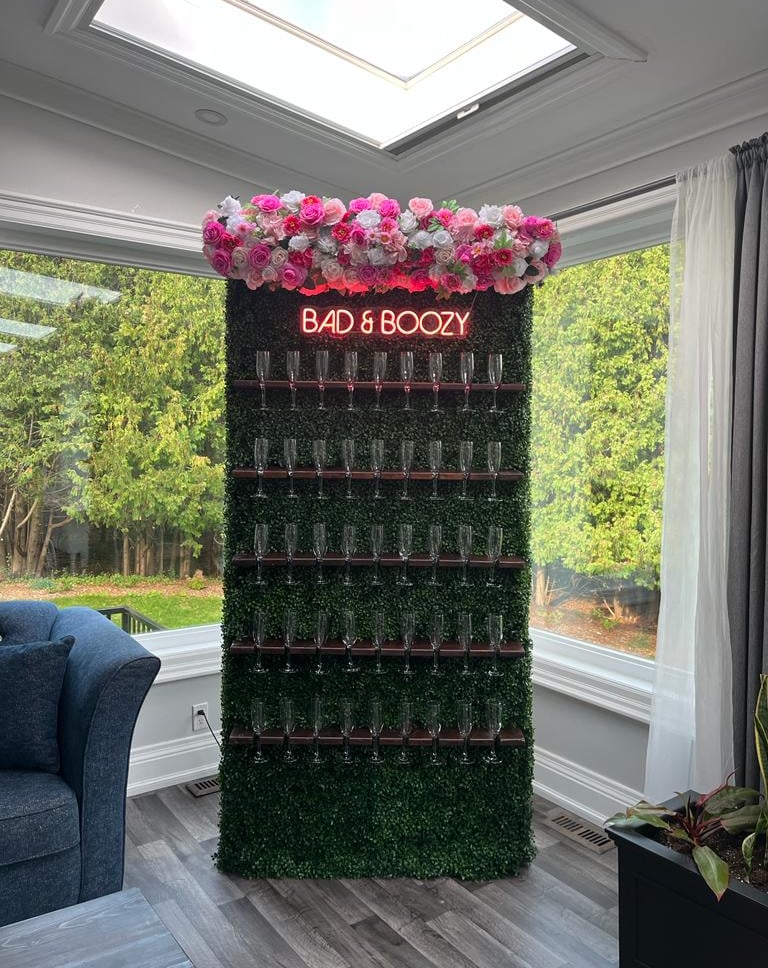 Champagne wall of assorted pink roses and a sign that says bad & Boozy