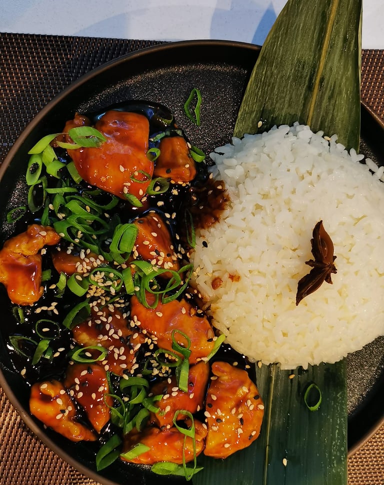 Bourbon Chicken mit Sesam und Frühlingszwiebeln auf Reis, dunkel fotografiert