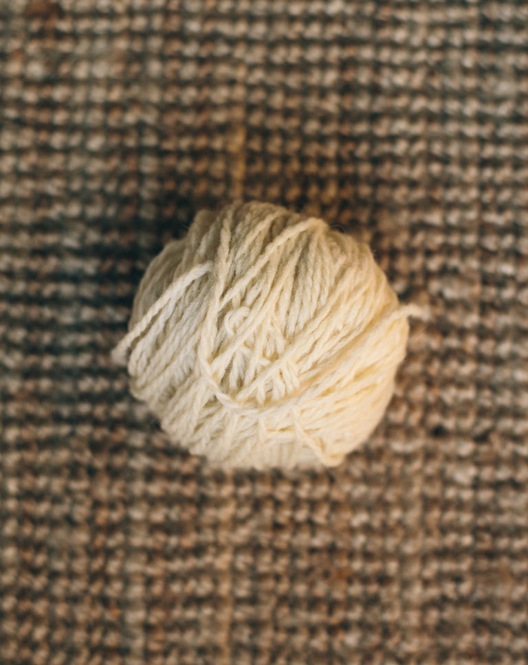 Nature morte d'une pelote de laine de pays écrue sur un fond de jute.