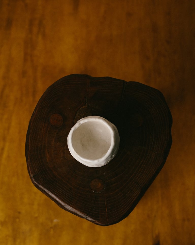 Vue plongeante sur un yunomi en grès blanc posé sur un tabouret en bois