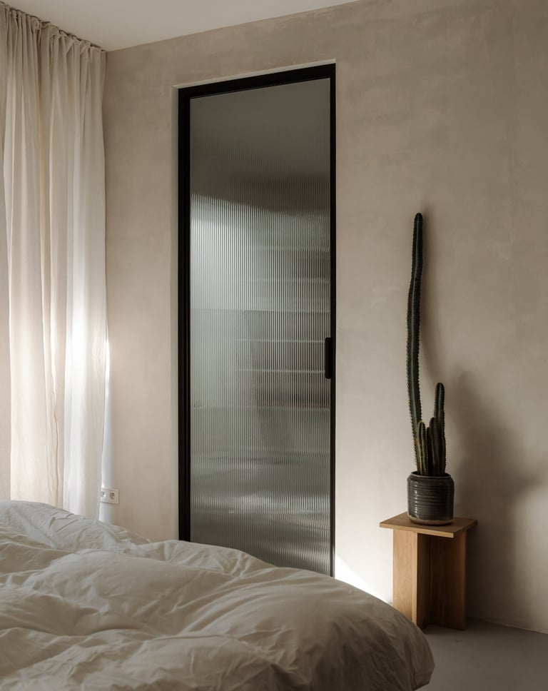 Bedroom with textured wall, fluted glass door, and white linens