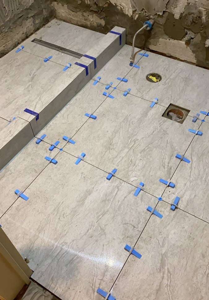 Pose de carrelage grand format avec croisillons autonivelants dans une salle de bain en rénovation