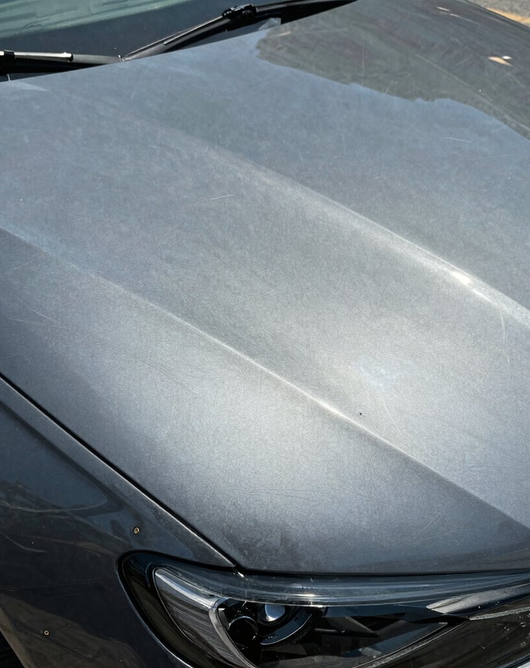 Close-up of a gray car hood showing visible swirl marks and paint scratches in the sunlight.