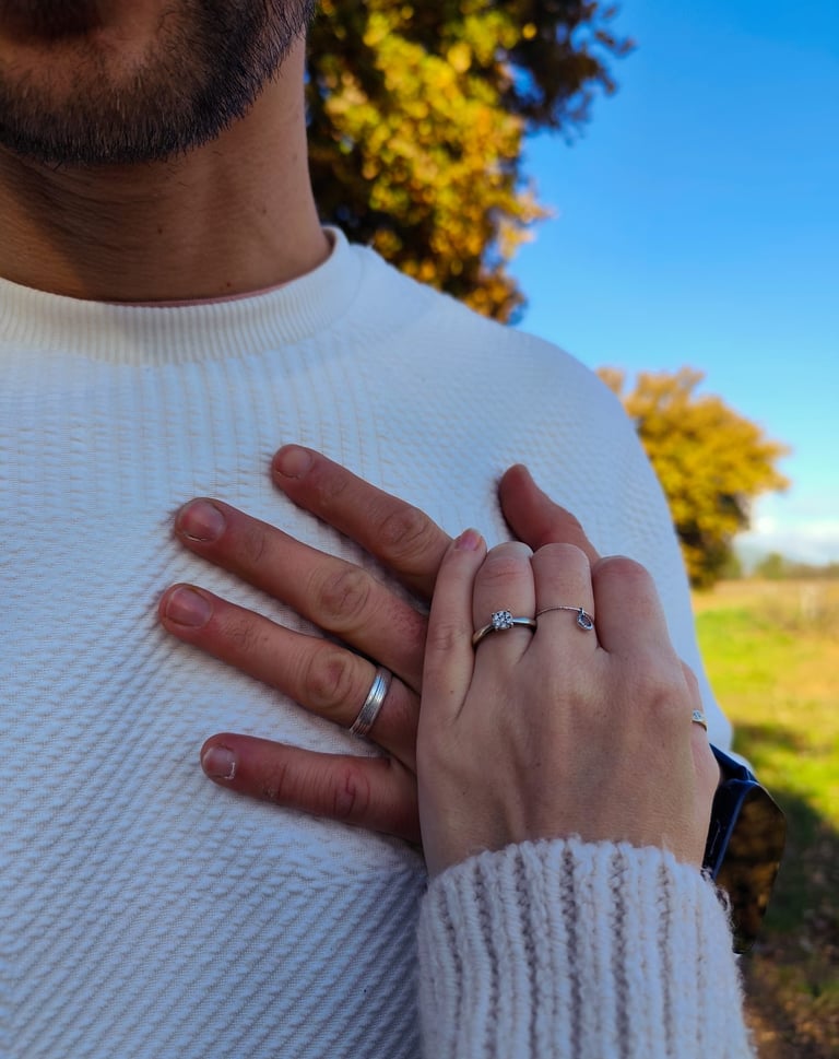 A close-up of a couple's hands with engagement and wedding rings outdoors during autumn.